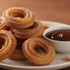 Crispy golden air fryer churros on a white plate with chocolate dipping sauce