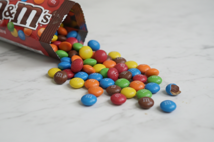 Colorful M&M candies spilling from a bag on white marble surface