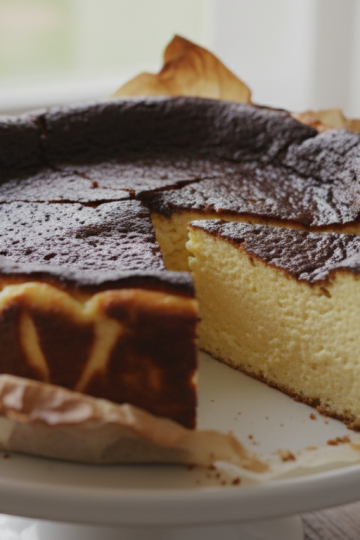 Basque burnt cheesecake on a white cake stand with dark caramelized top and creamy interior