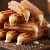Creme-filled churros on a dark wooden board dusted in cinnamon sugar with pastry cream filling visible