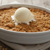 Golden apple crisp in white baking dish with vanilla ice cream