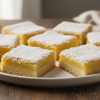 Classic homemade lemon bars dusted with powdered sugar on white plate with fresh lemon slices