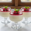 Three elegant vanilla panna cottas in glass cups topped with raspberry coulis and mint