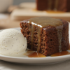 Sticky toffee pudding on a plate drenched in warm toffee sauce with vanilla ice cream